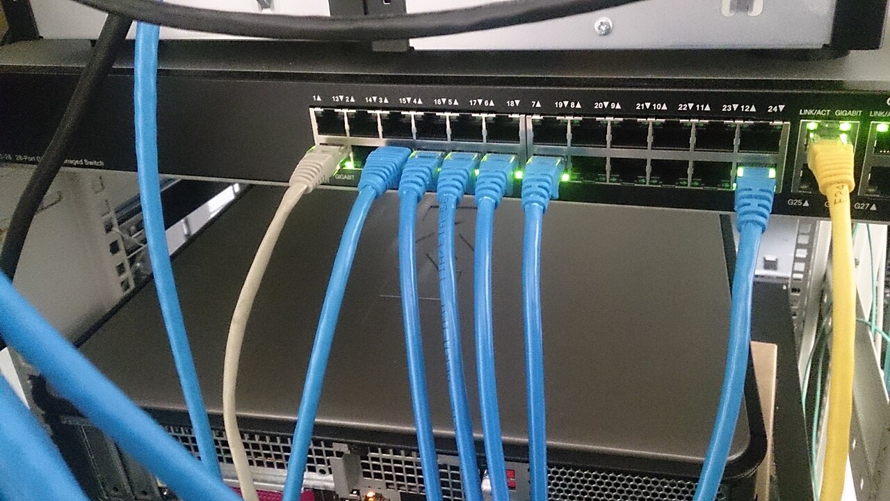 Сетевой коммутатор с подключёнными синими Ethernet-кабелями и светящимися индикаторами портов